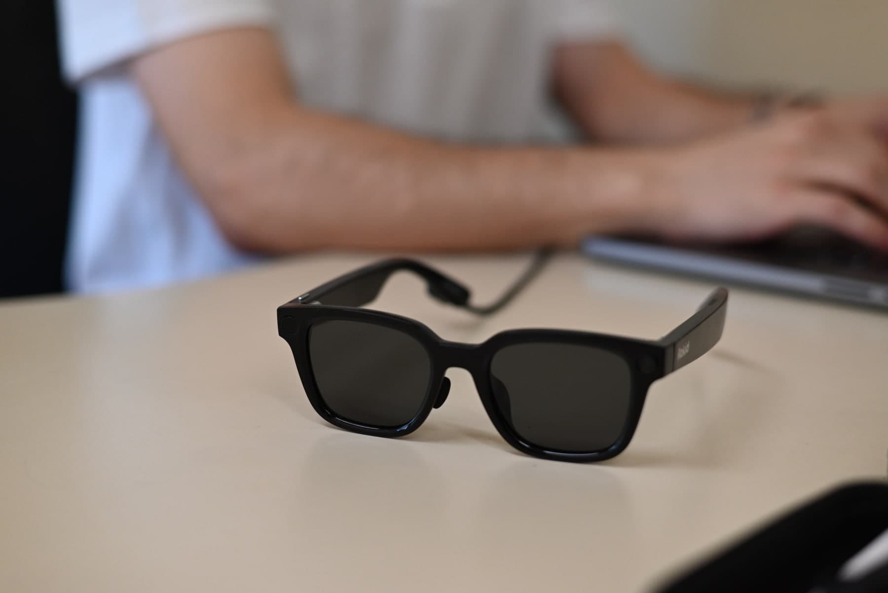 SparkVision smart glasses charging on a desk while a team member works at a laptop.